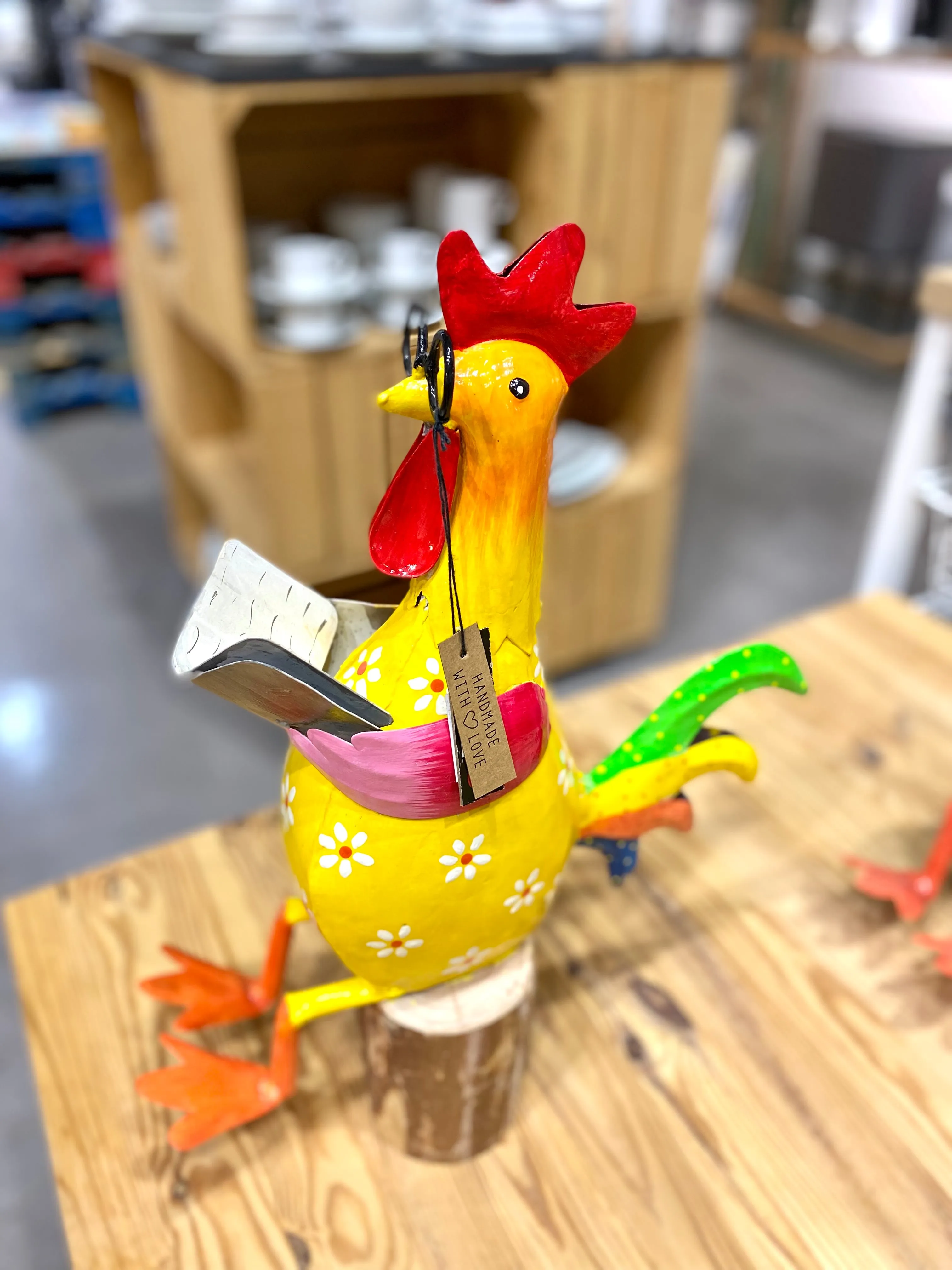 Gallo sentado sobre tronco, en metal de alegres y coloridos tonos.