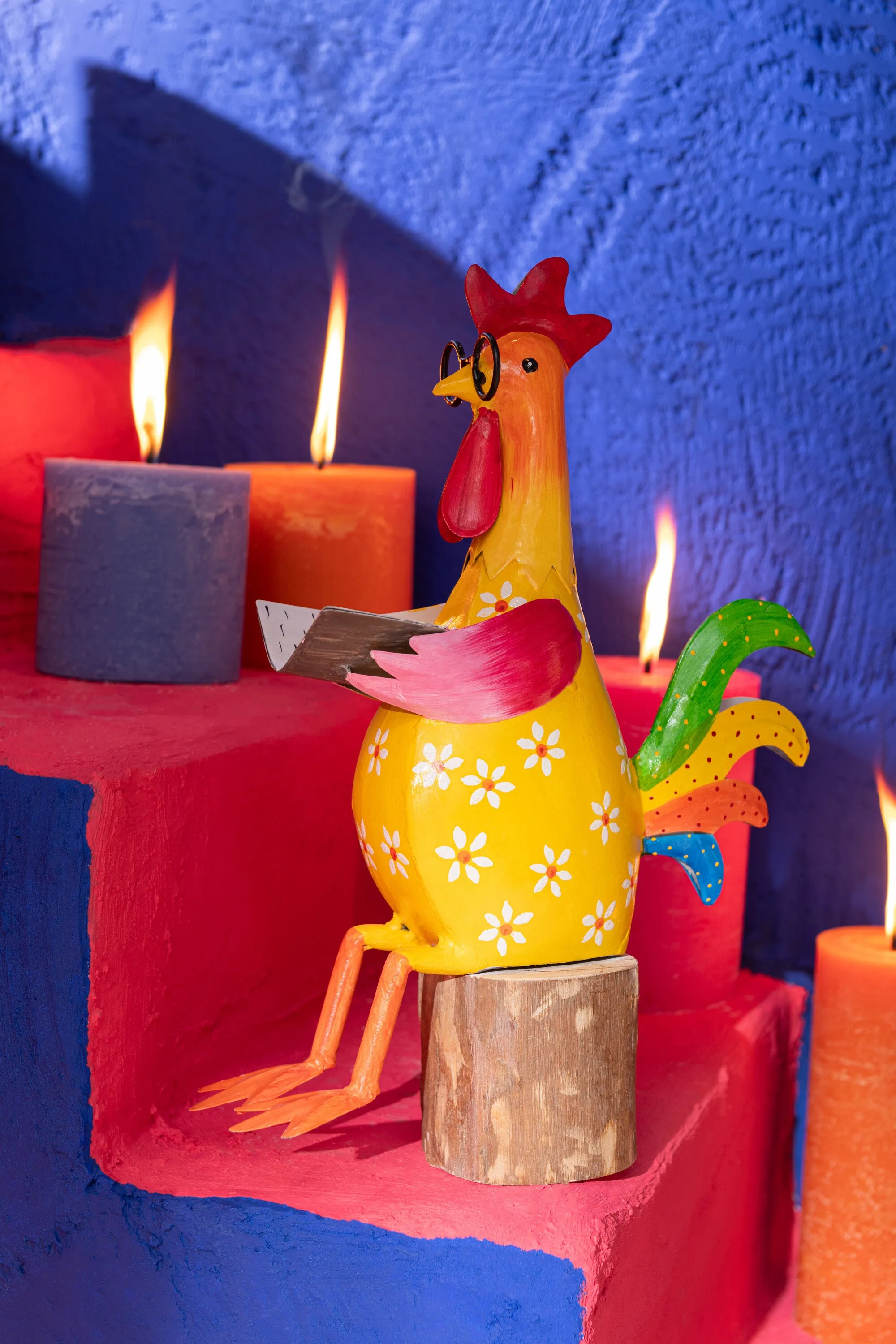 Gallo sentado sobre tronco, en metal de alegres y coloridos tonos.