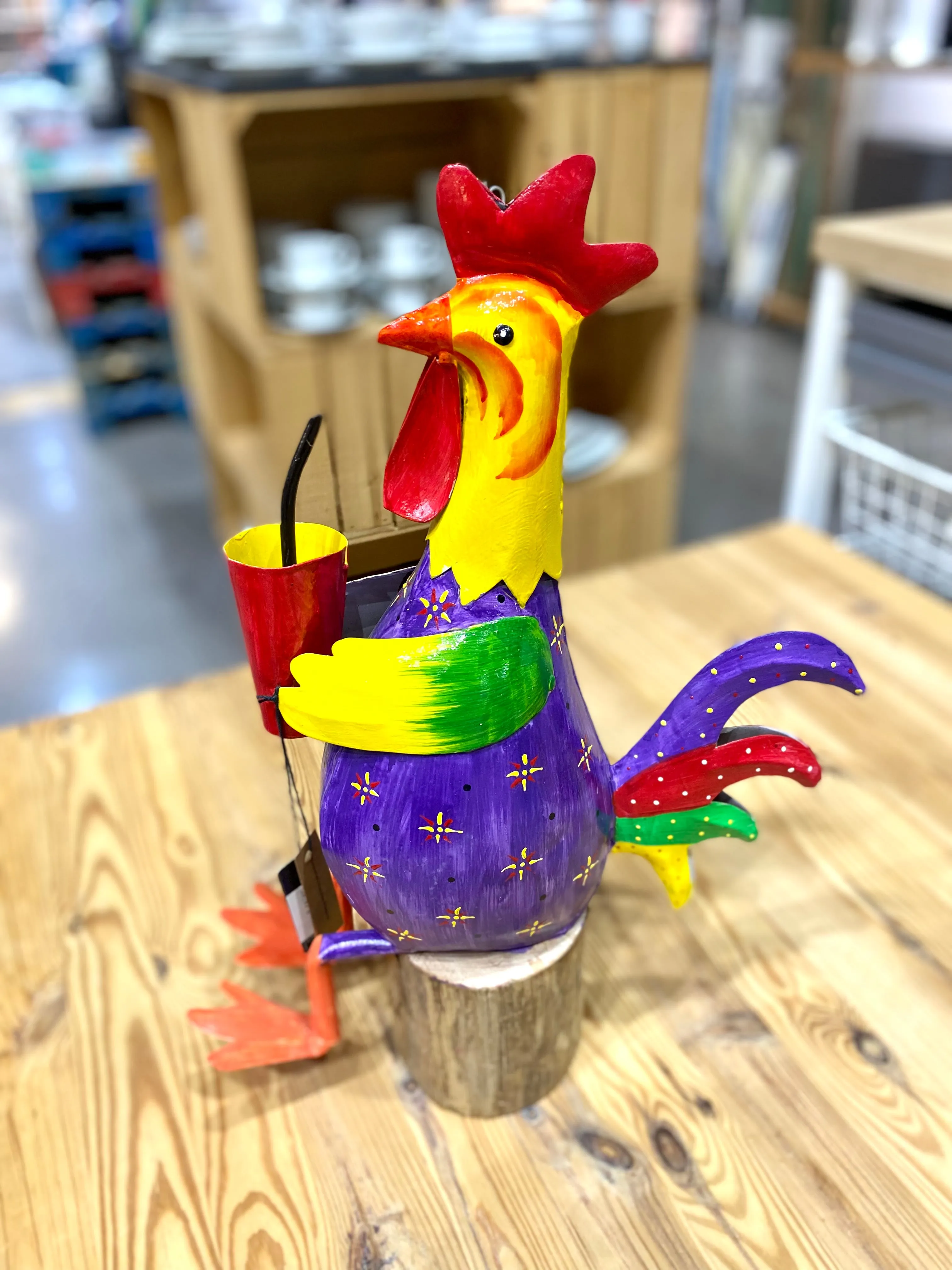 Gallo sentado sobre tronco, en metal de alegres y coloridos tonos.