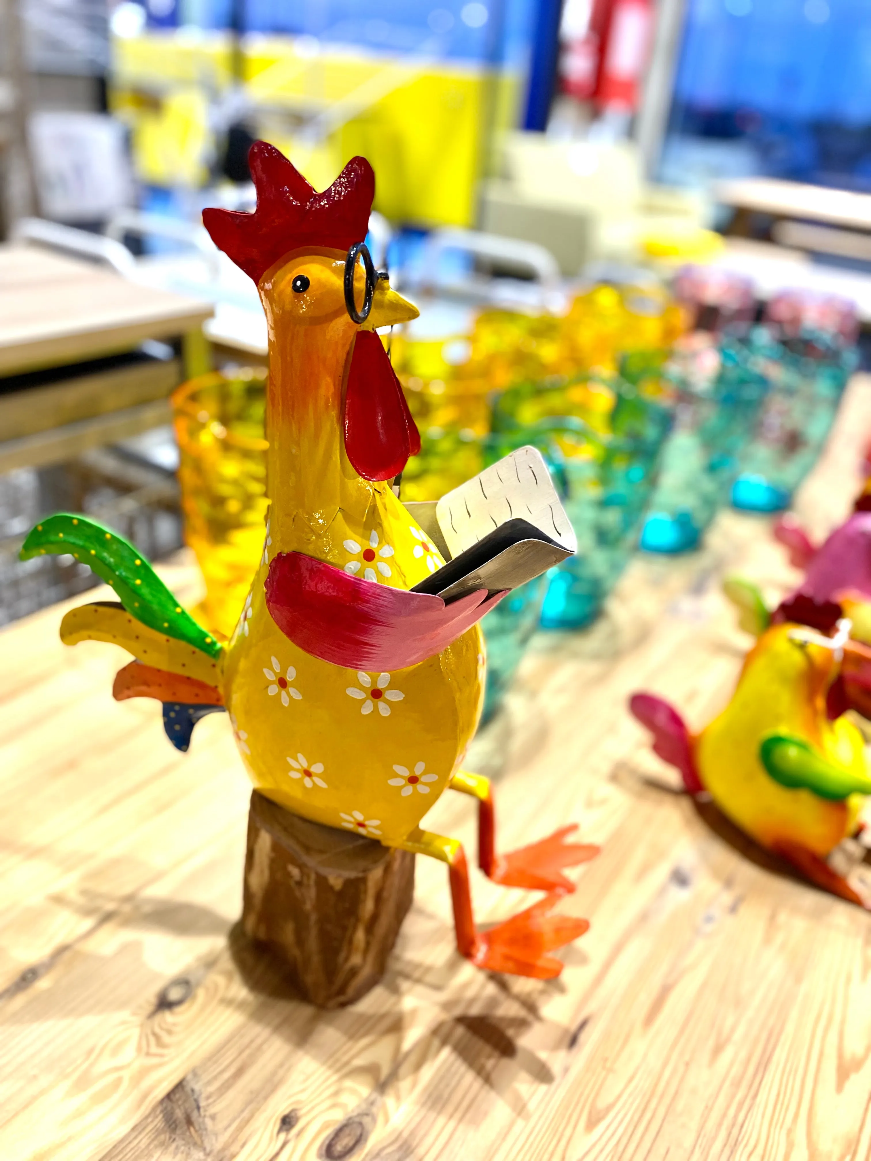 Gallo sentado sobre tronco, en metal de alegres y coloridos tonos.